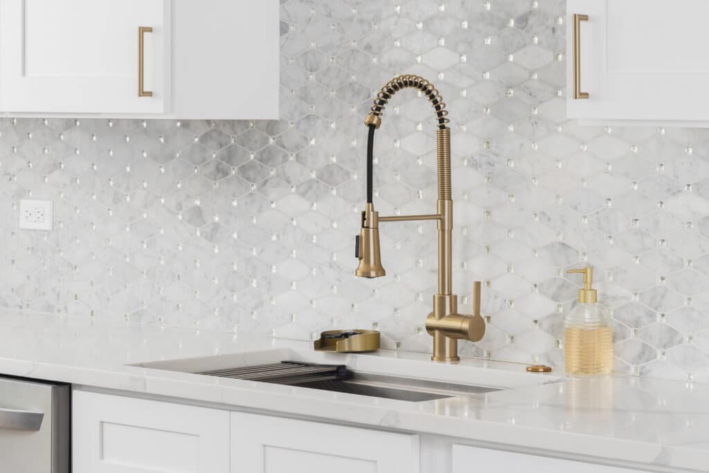 Cuisine moderne : robinet laiton brossé, évier inox, comptoir marbre blanc et dosseret mosaïque hexagone incrusté de cristaux.