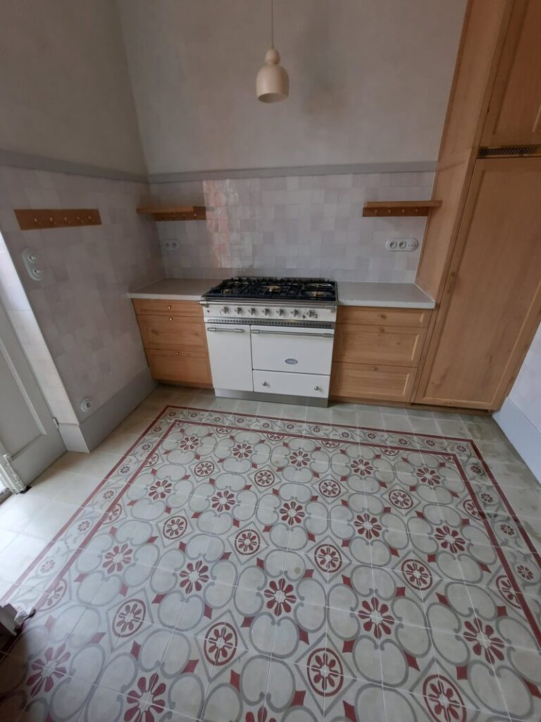 Cuisine charme : carreaux, bois et cuisinière vintage Cuisine lumineuse avec sol en carreaux de ciment rouge et gris, cuisinière Aga blanche, et placards en bois clair.